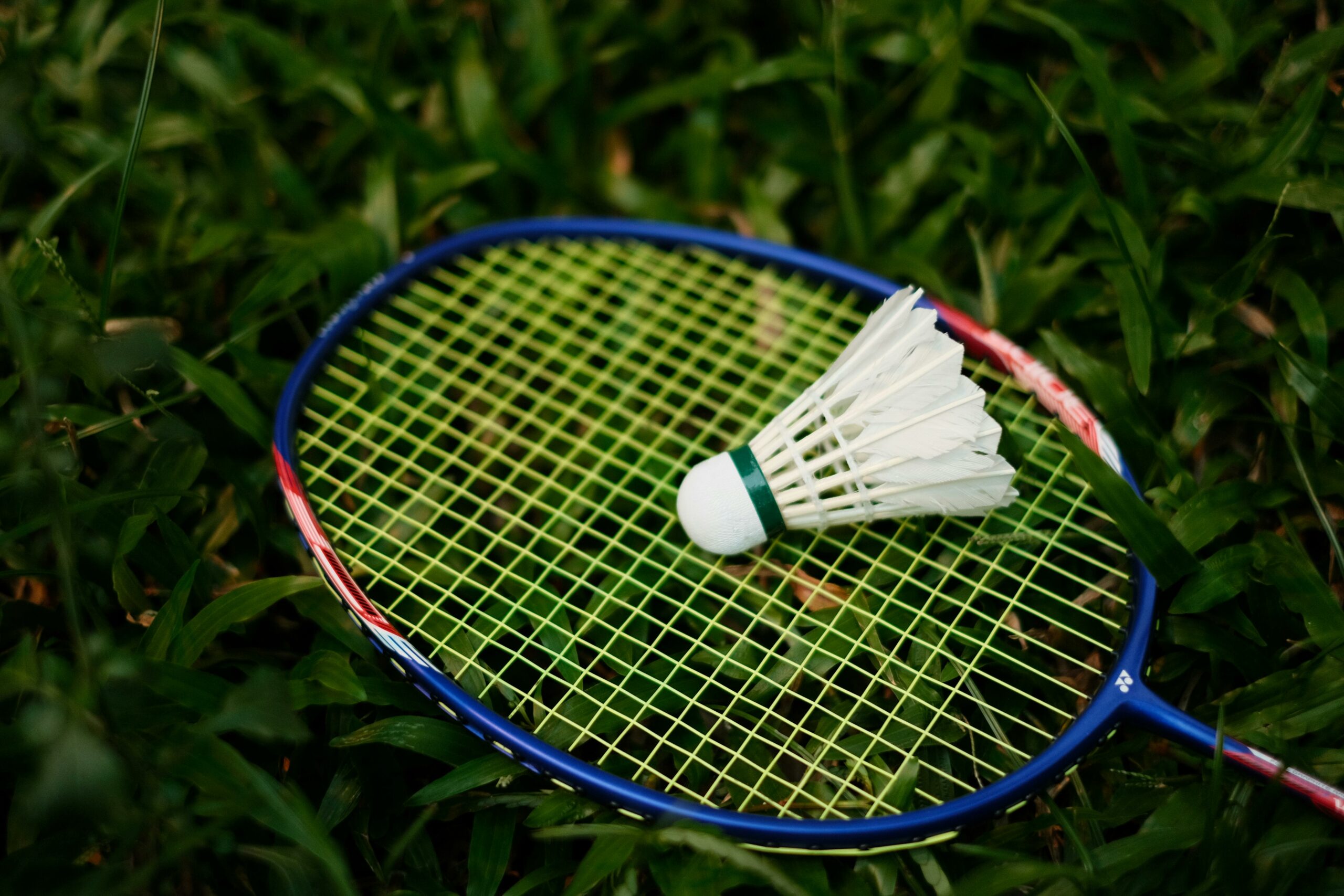 Close-up of a badminton racket and shuttlecock on grass, embodying the spirit of outdoor sports.