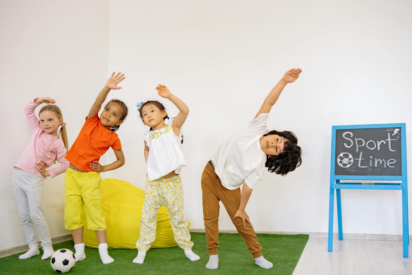 Joyful children stretching during indoor sport time in a classroom.